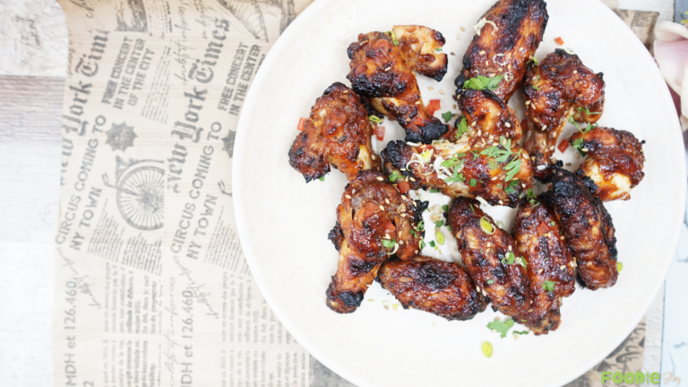 Sticky glazed chicken wings topped with scallions, cilantro, and sesame seeds on a plate