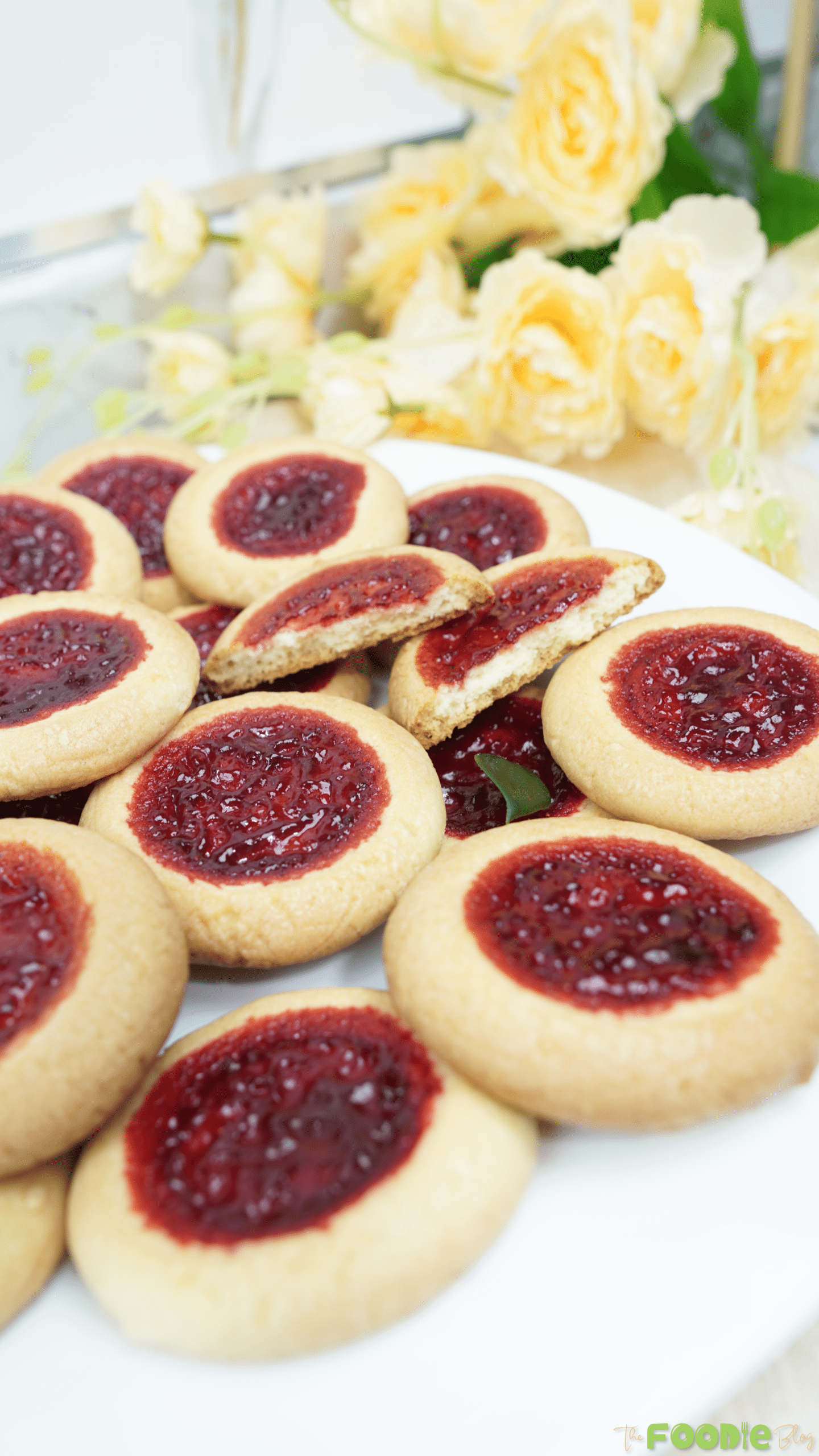 Close-up of thumbprint cookies with glossy strawberry jam centers on a white plate