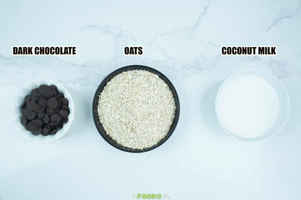 Overhead view of dark chocolate, quick oats, and coconut milk labeled on a white surface