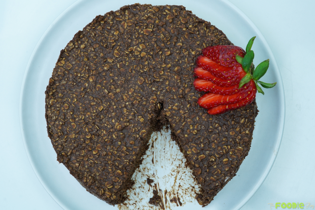 Overhead view of chocolate oatmeal cake with a slice removed and strawberries on top