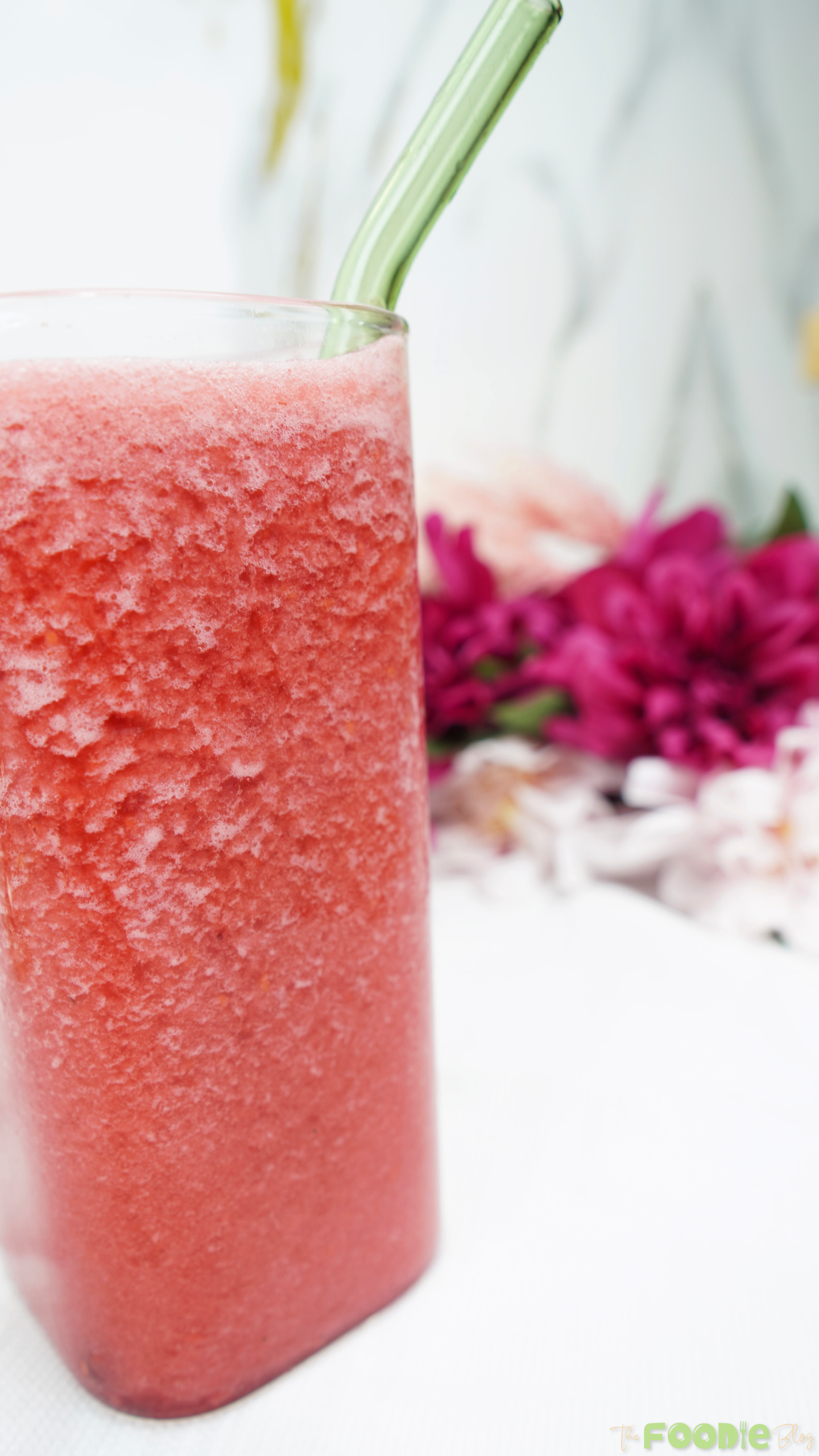 Tall glass of blended raspberry juice with a straw on a white surface