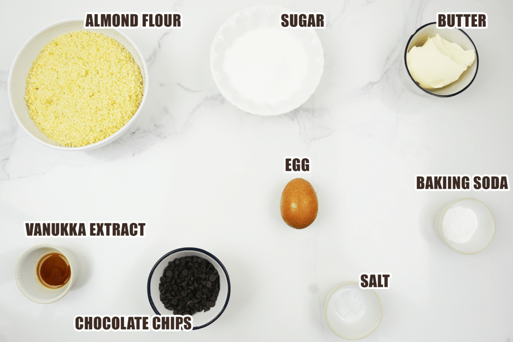 Overhead ingredients for almond flour chocolate chip cookies including almond flour, sugar, butter, egg, vanilla, baking soda, salt, and chocolate chips
