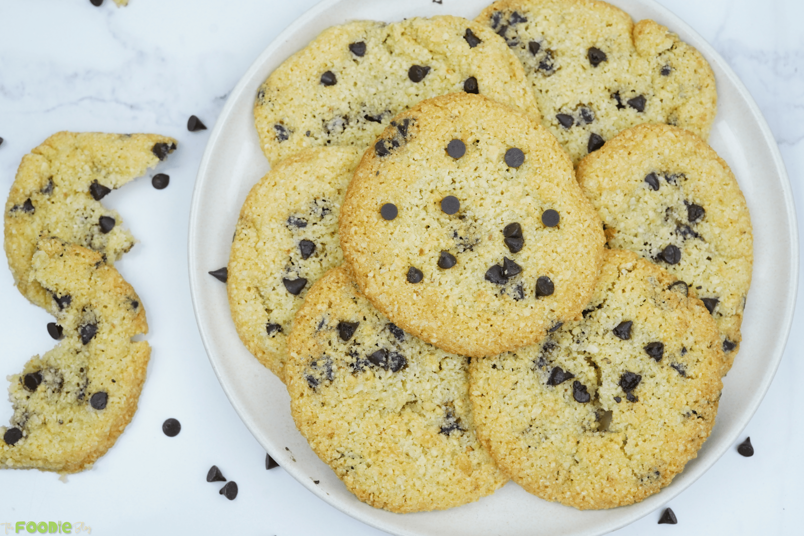 Overhead view of almond flour chocolate chip cookies arranged on a plate with a broken cookie on the side