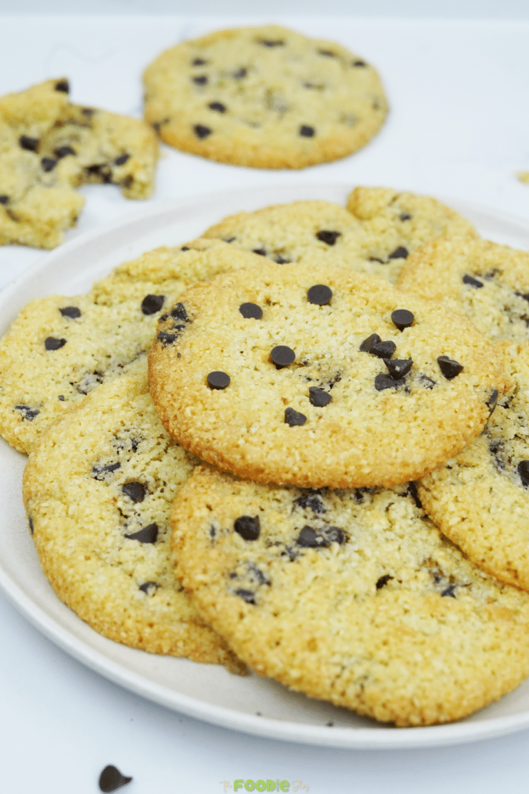 Almond flour chocolate chip cookies stacked on a plate with extra cookies in the background