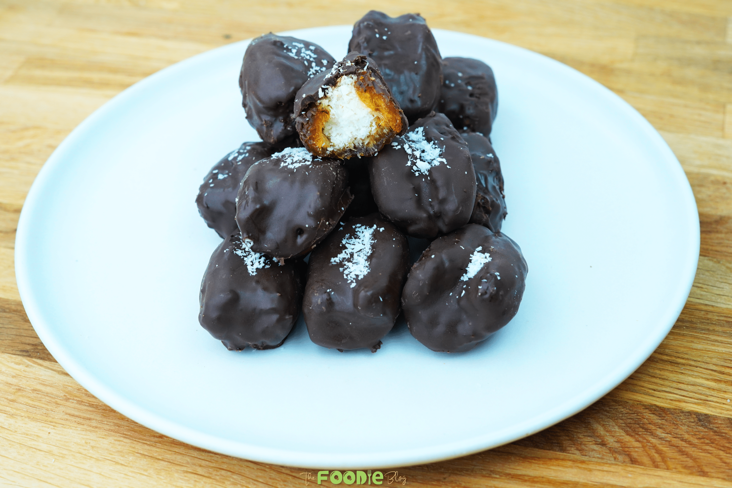 Chocolate-covered Bounty Dates piled on a plate with a bite showing coconut filling