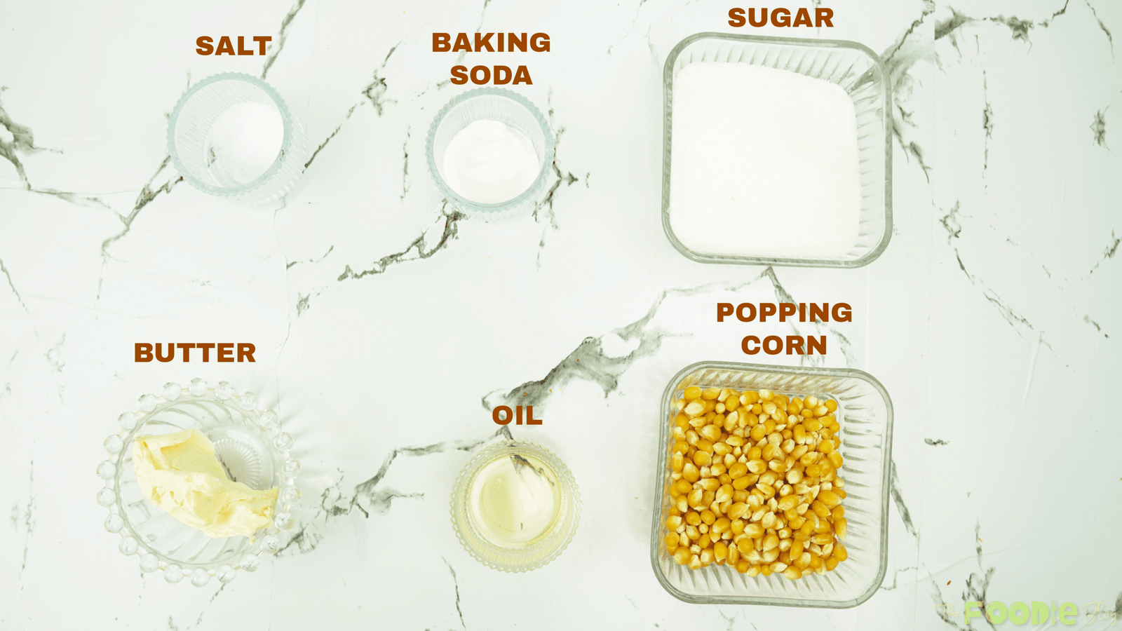 Overhead view of caramel popcorn ingredients including popcorn kernels, sugar, butter, oil, salt, and baking soda.