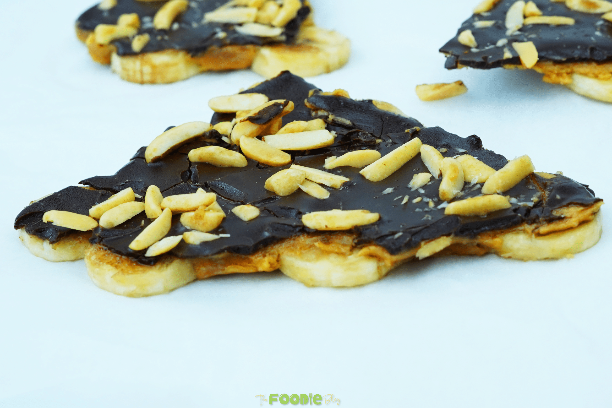 Close-up of chocolate banana bark topped with crushed peanuts on a white surface
