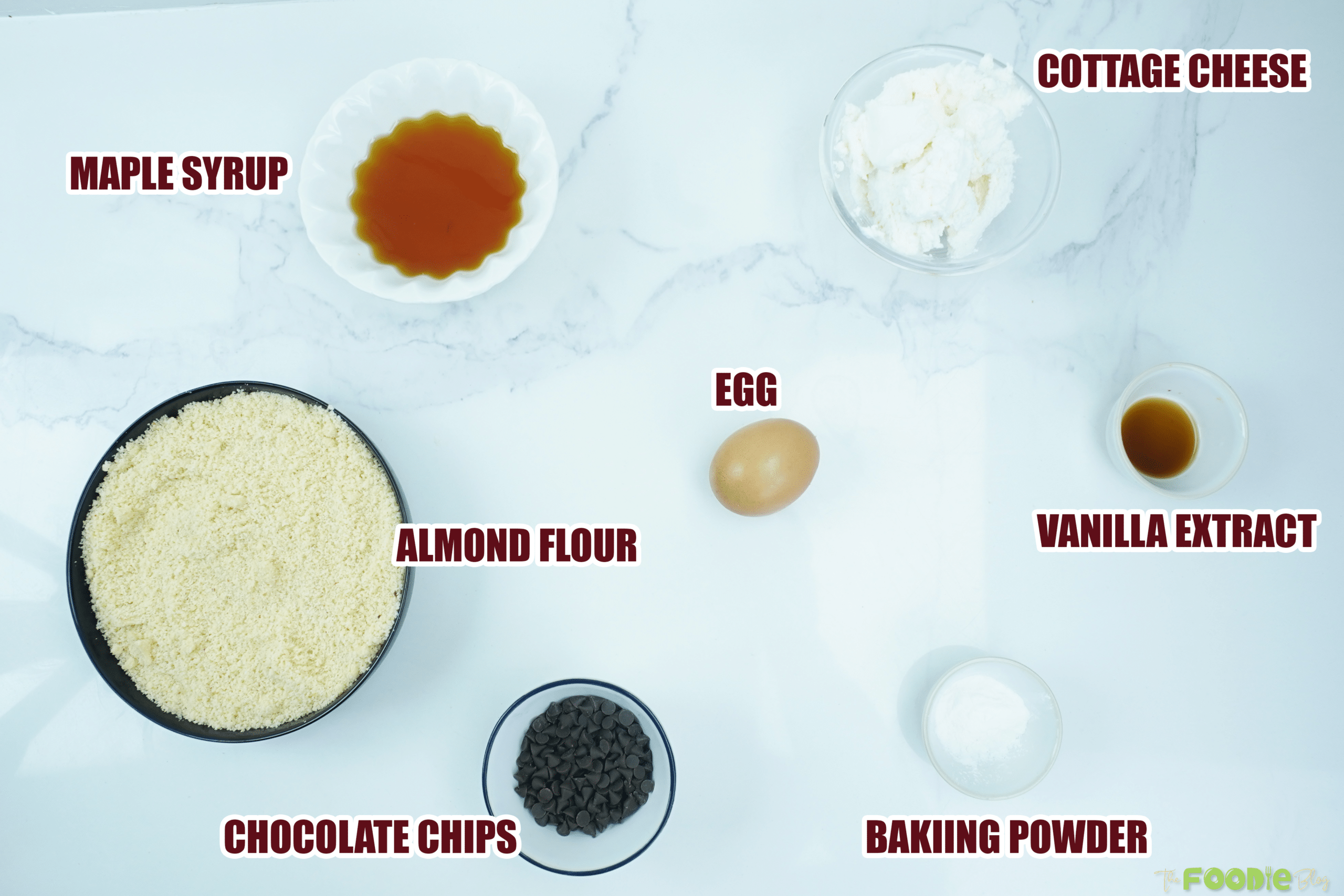 Ingredients laid out for cottage cheese chocolate chip cookies, including almond flour, cottage cheese, egg, maple syrup, and chocolate chips