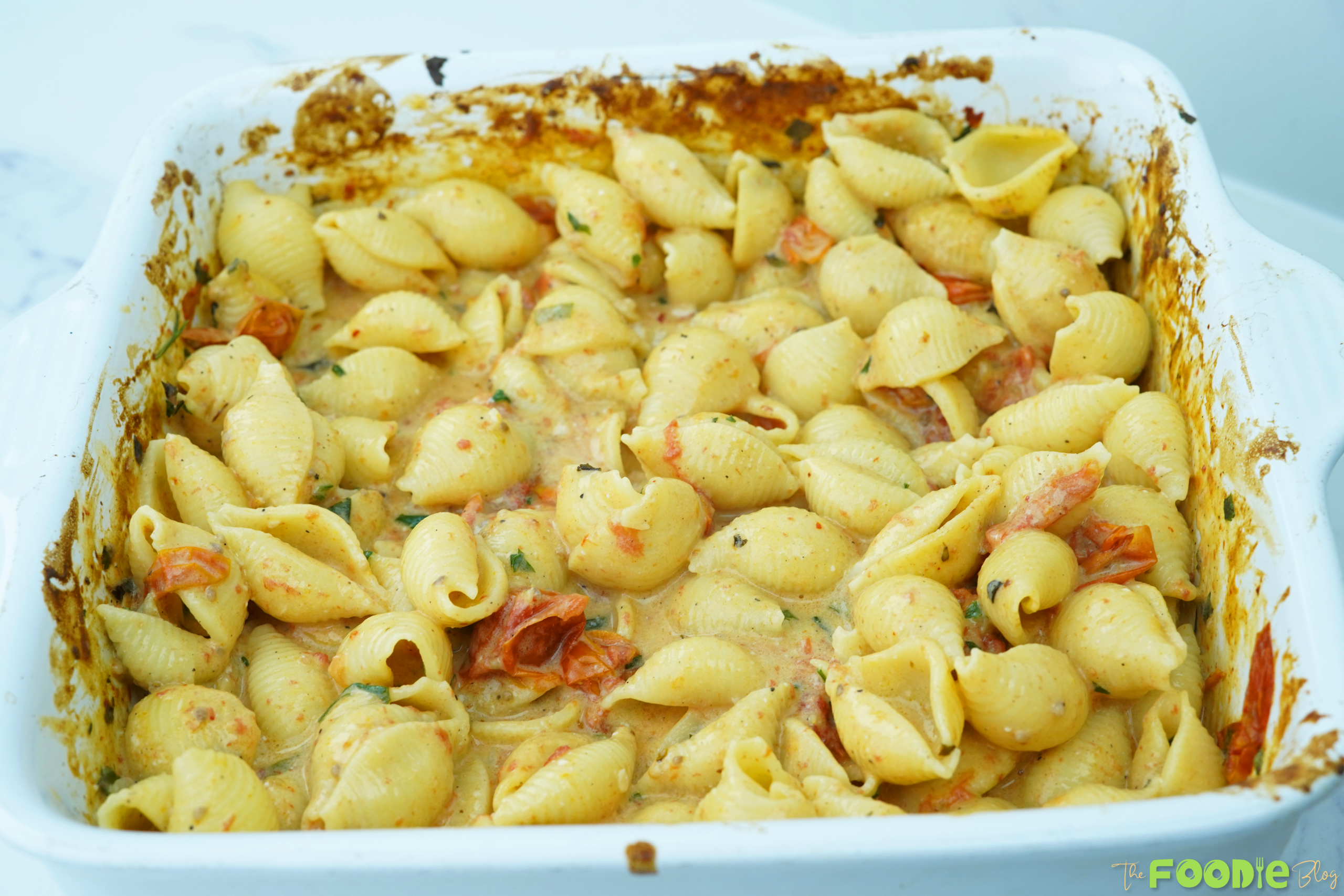 Baked feta pasta mixed in a baking dish with creamy sauce and roasted cherry tomatoes