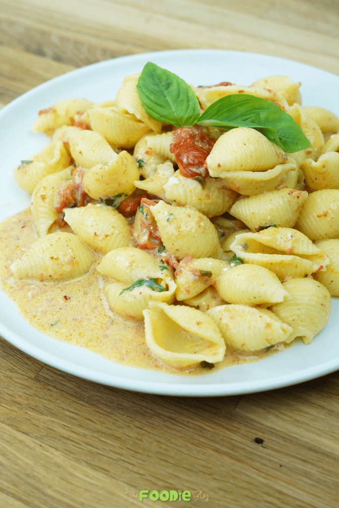 Creamy feta pasta shells with cherry tomatoes and fresh herbs on a white plate.