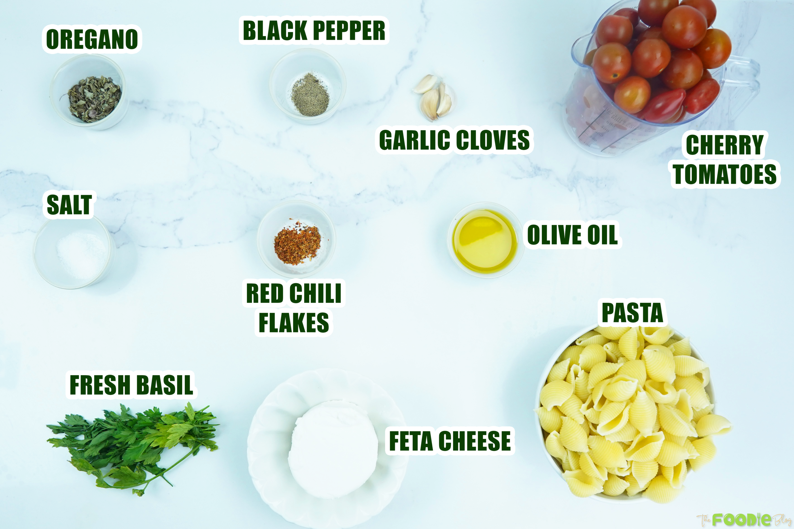 Ingredients laid out for feta cheese pasta including pasta shells, cherry tomatoes, feta, olive oil, garlic, oregano, and basil