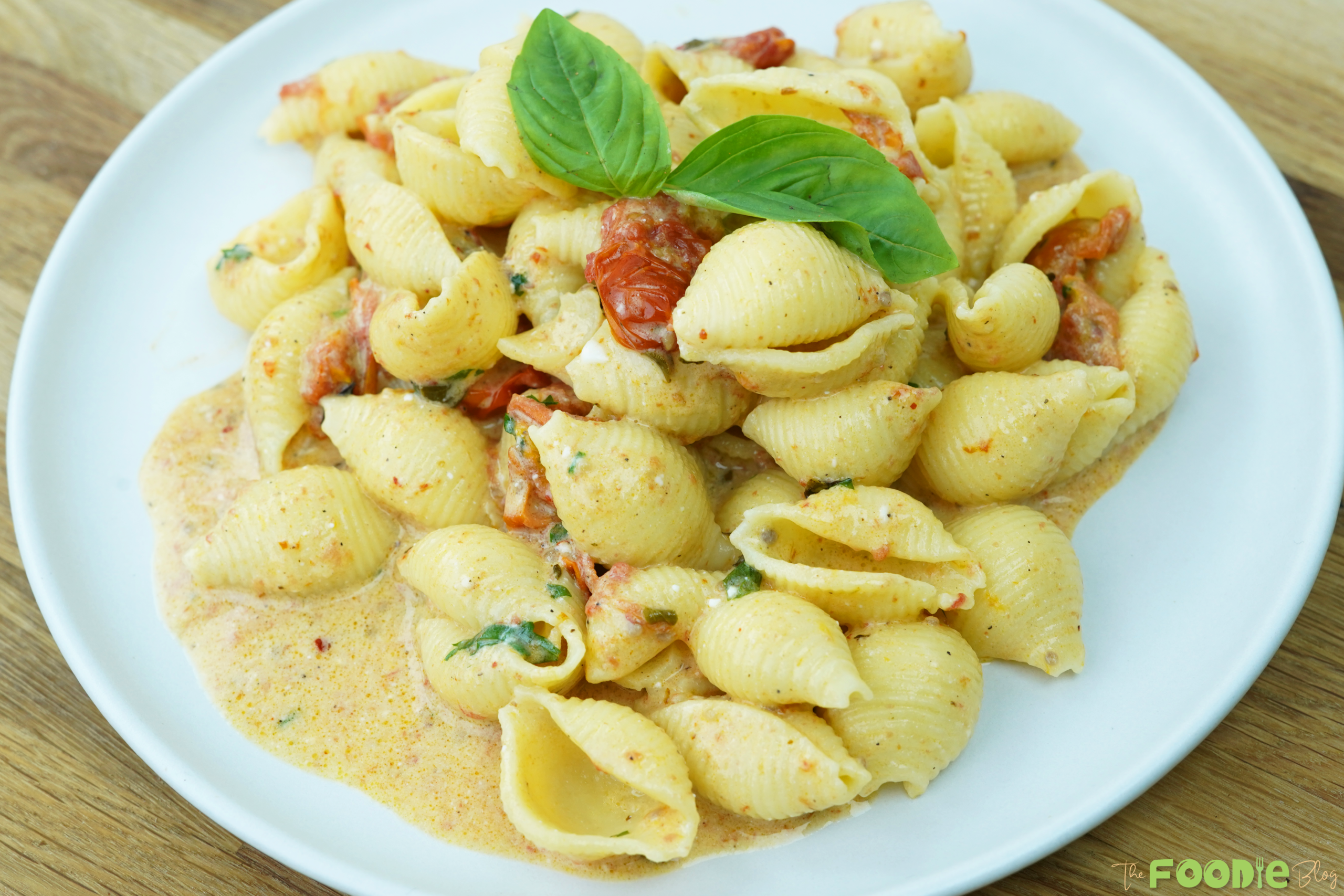 Overhead view of creamy pasta shells with baked feta tomato sauce and basil on a plate