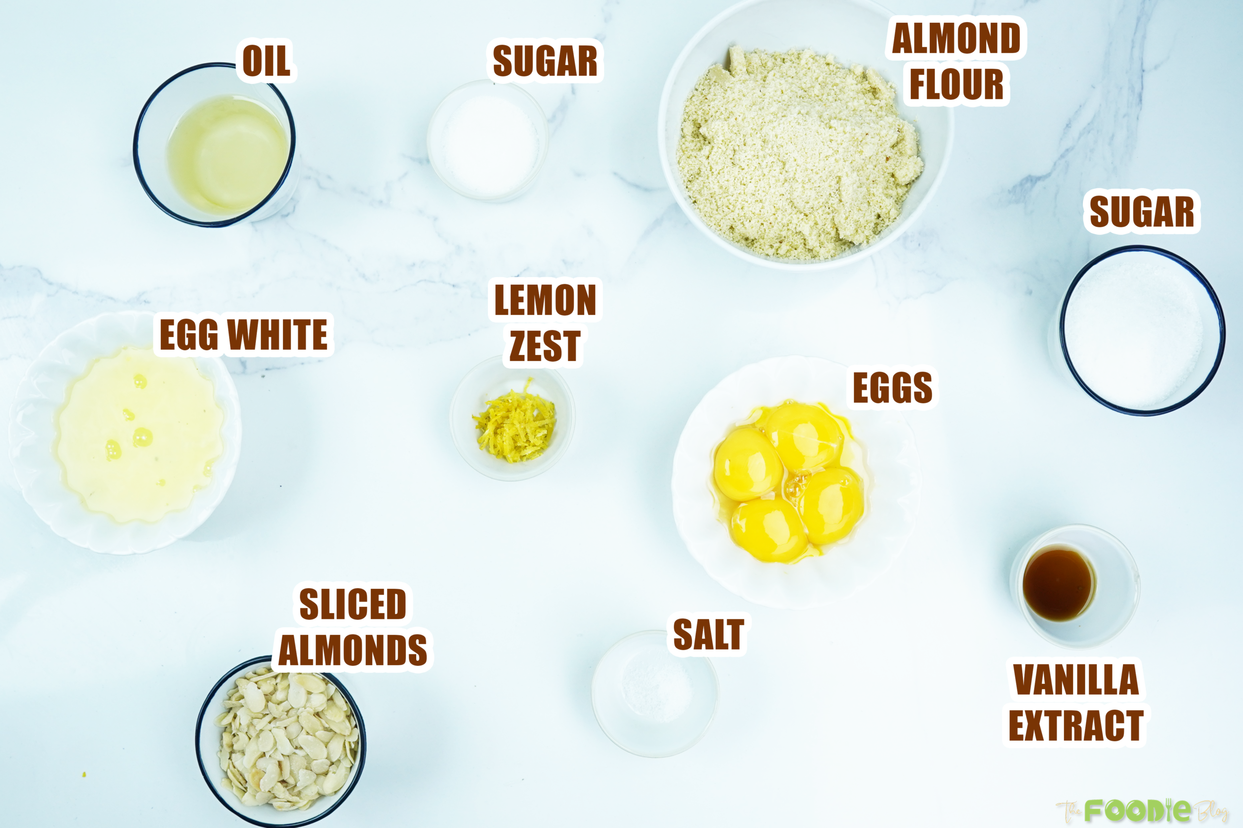 Overhead view of eggs, almond flour, sugar, lemon zest, vanilla, oil, salt, and sliced almonds
