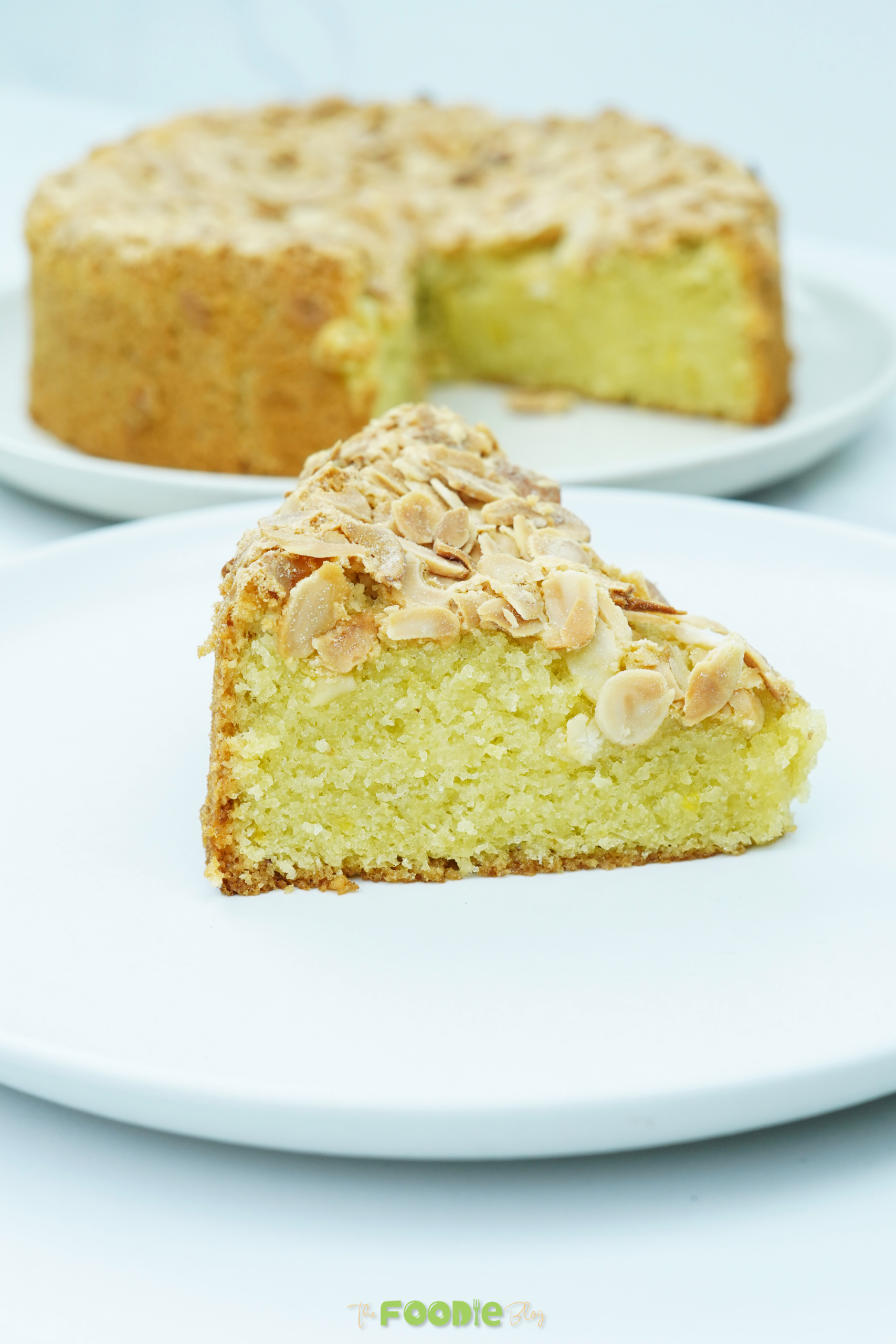 Single slice of flourless almond cake on a plate with the remaining cake blurred in the background