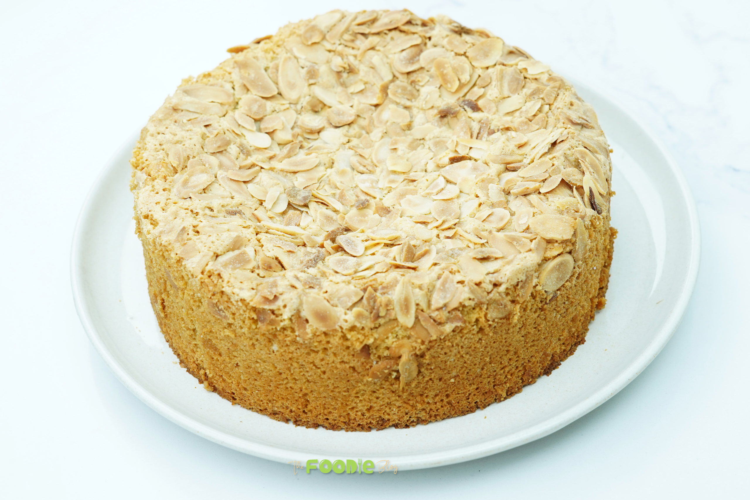Whole flourless almond cake topped with sliced almonds on a white plate