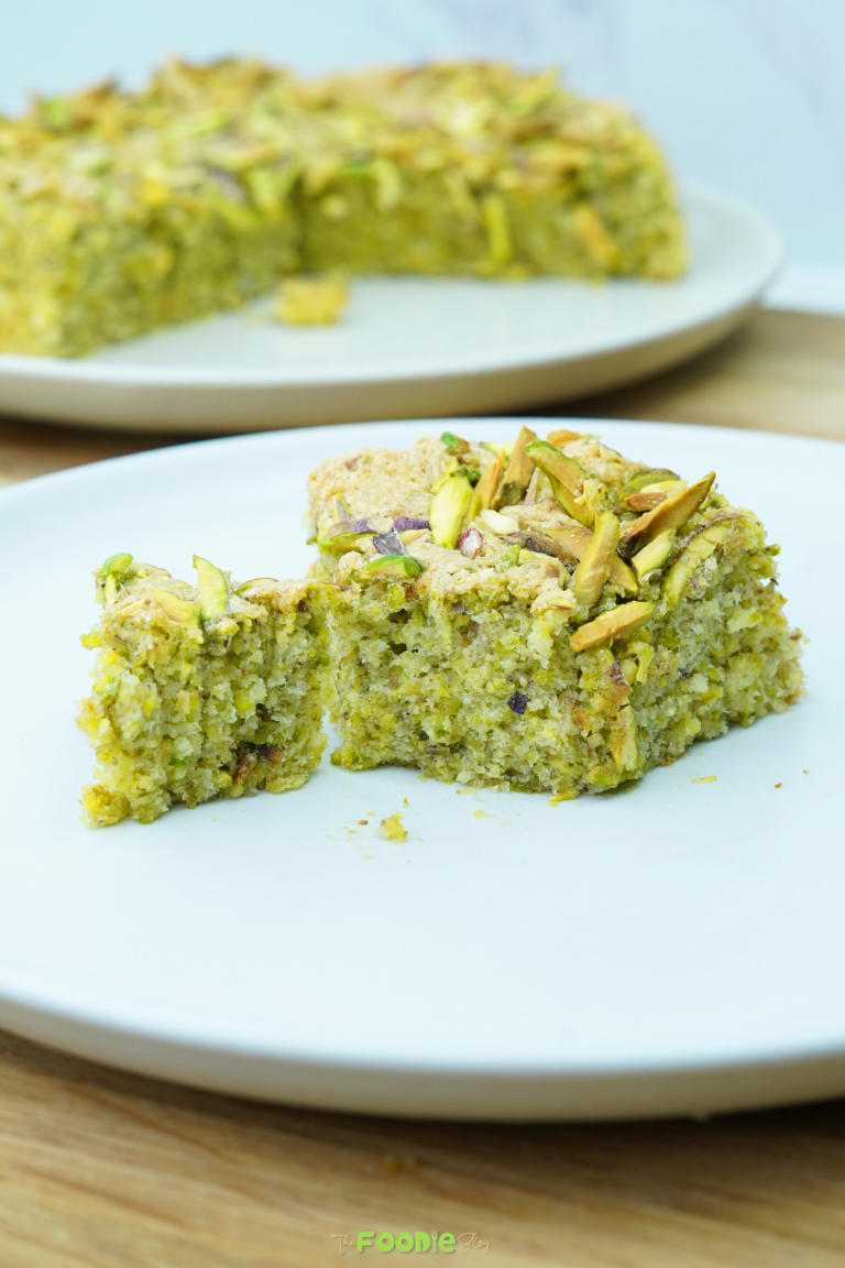 Fork holding a bite of pistachio cake with chopped pistachios scattered on top
