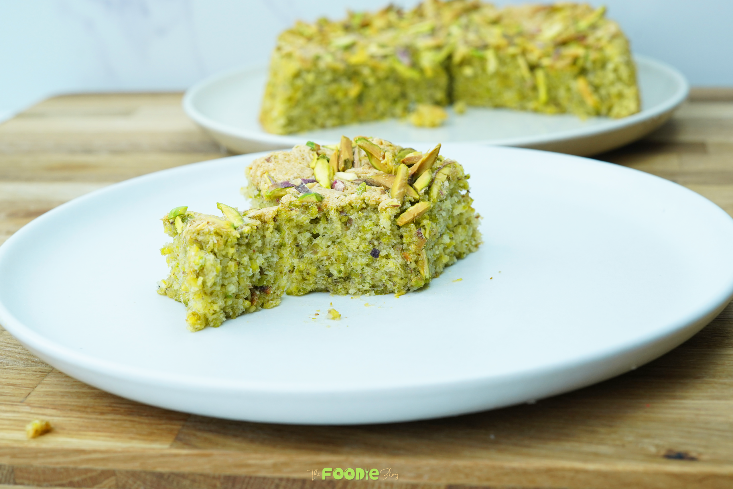 Plated slice of pistachio cake with a green crumb and pistachio topping
