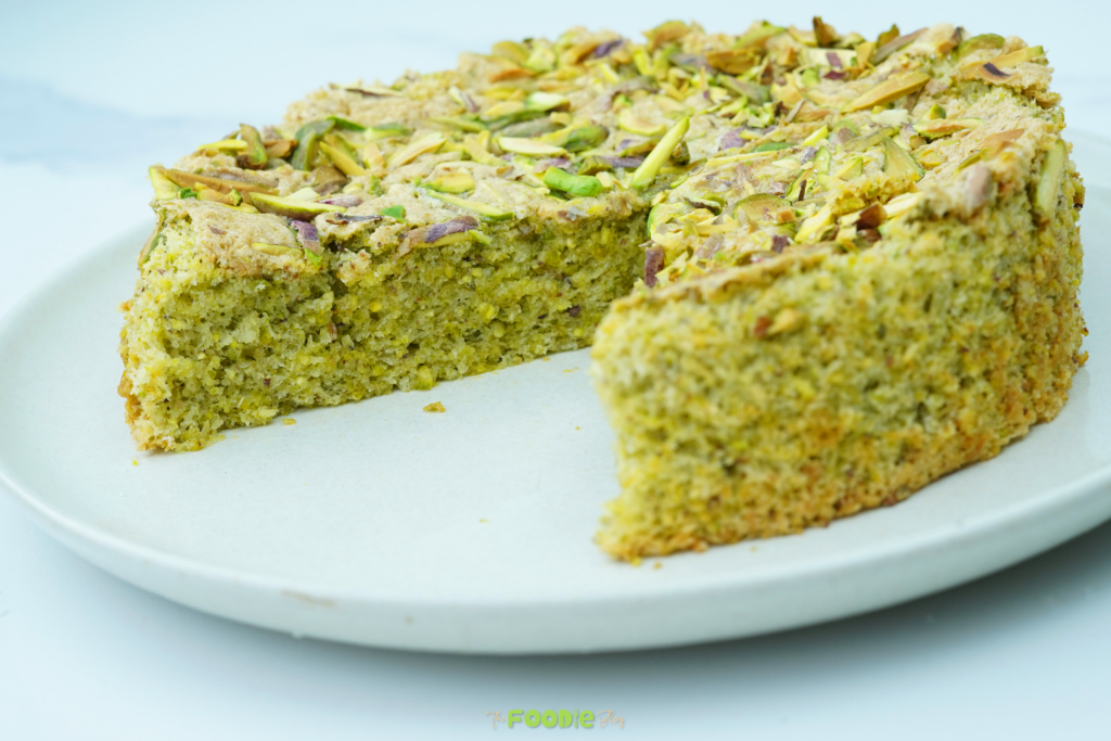 Close-up of a slice of pistachio cake with a chopped pistachio topping on a white plate