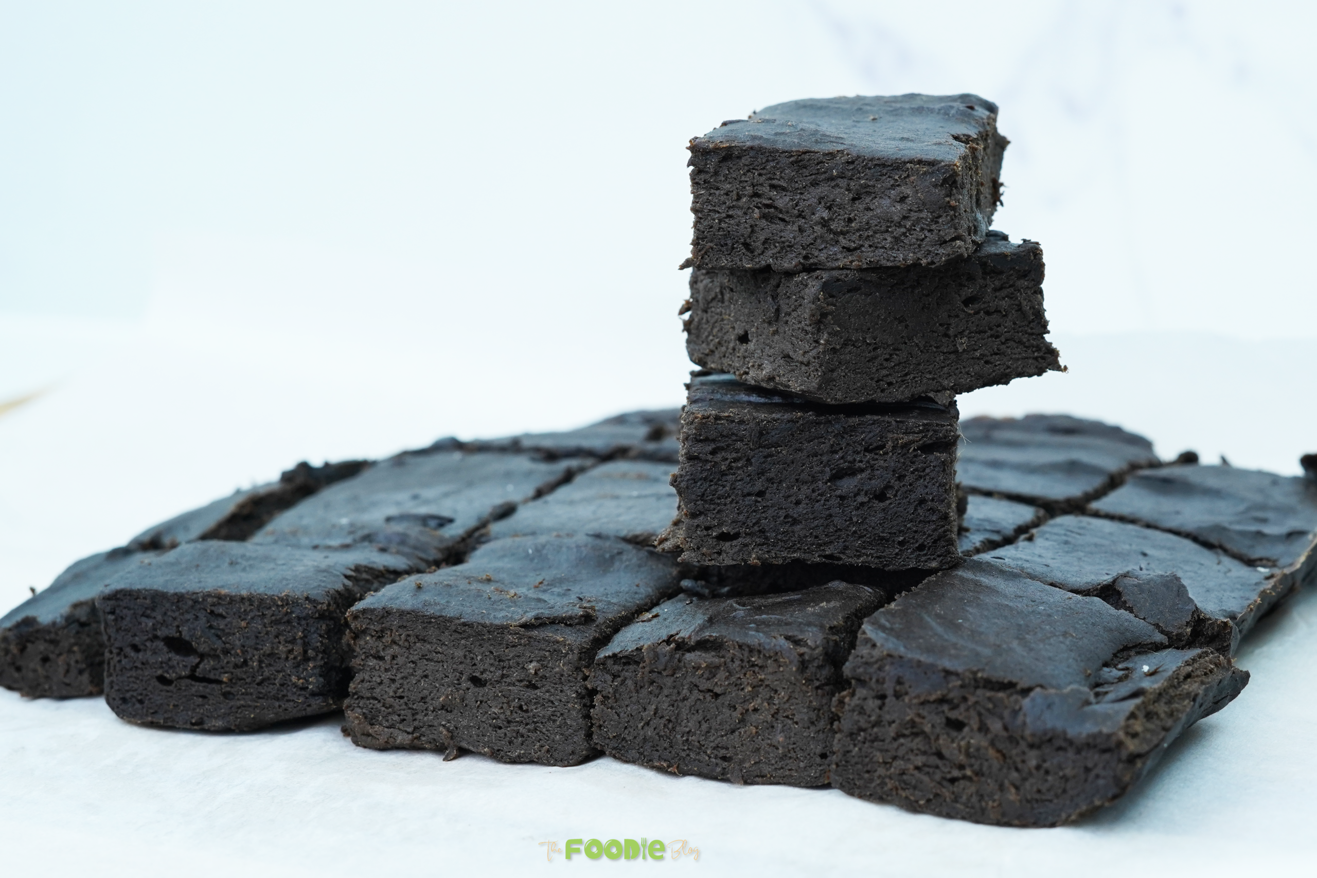 Stacked squares of dark no-bake brownies on a parchment-lined surface
