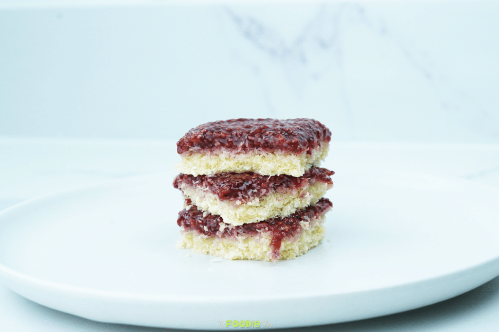 Three coconut raspberry bars stacked on a white plate