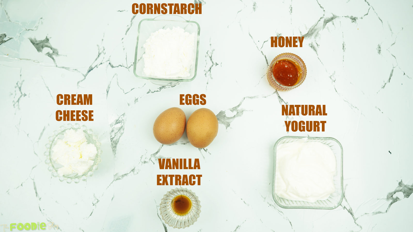 Eggs, yogurt, cornstarch, honey, vanilla, and cream cheese on a marble surface
