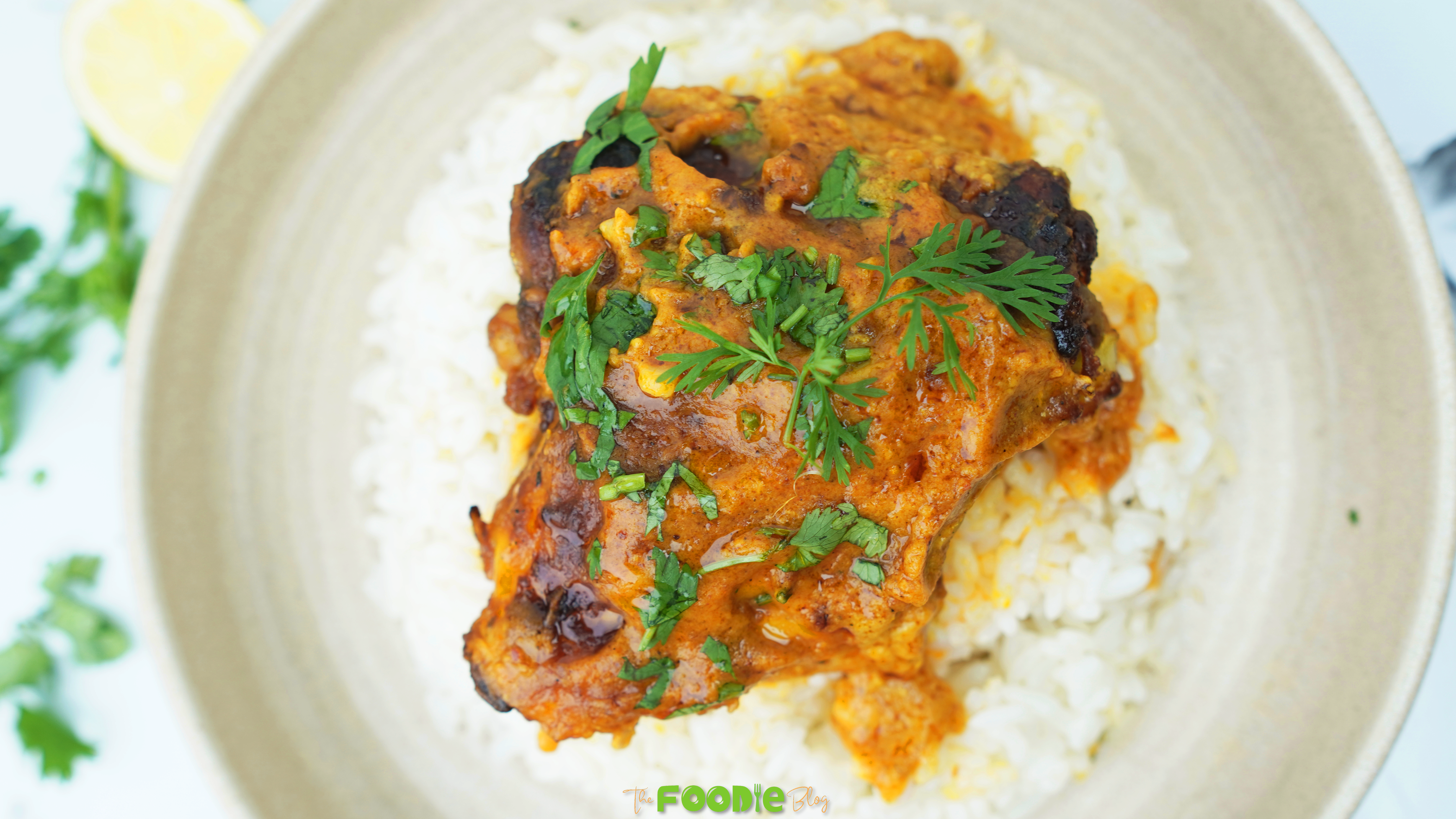 Butter chicken thigh served over basmati rice with fresh cilantro and a lemon wedge nearby