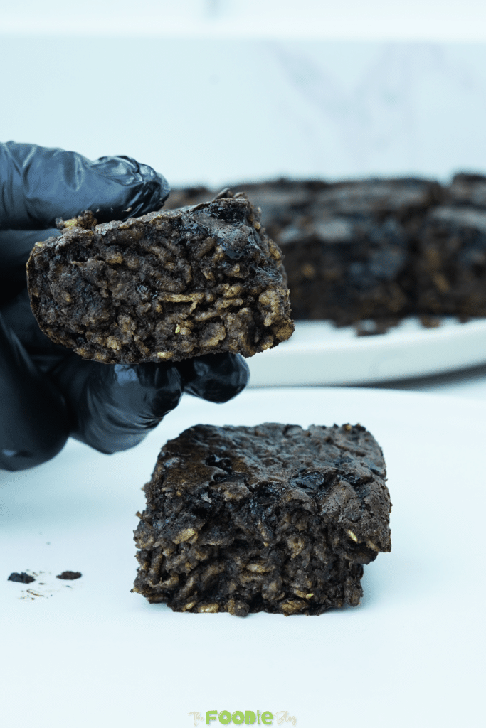 Hand holding a fudgy oatmeal brownie square with oats and chocolatey crumb