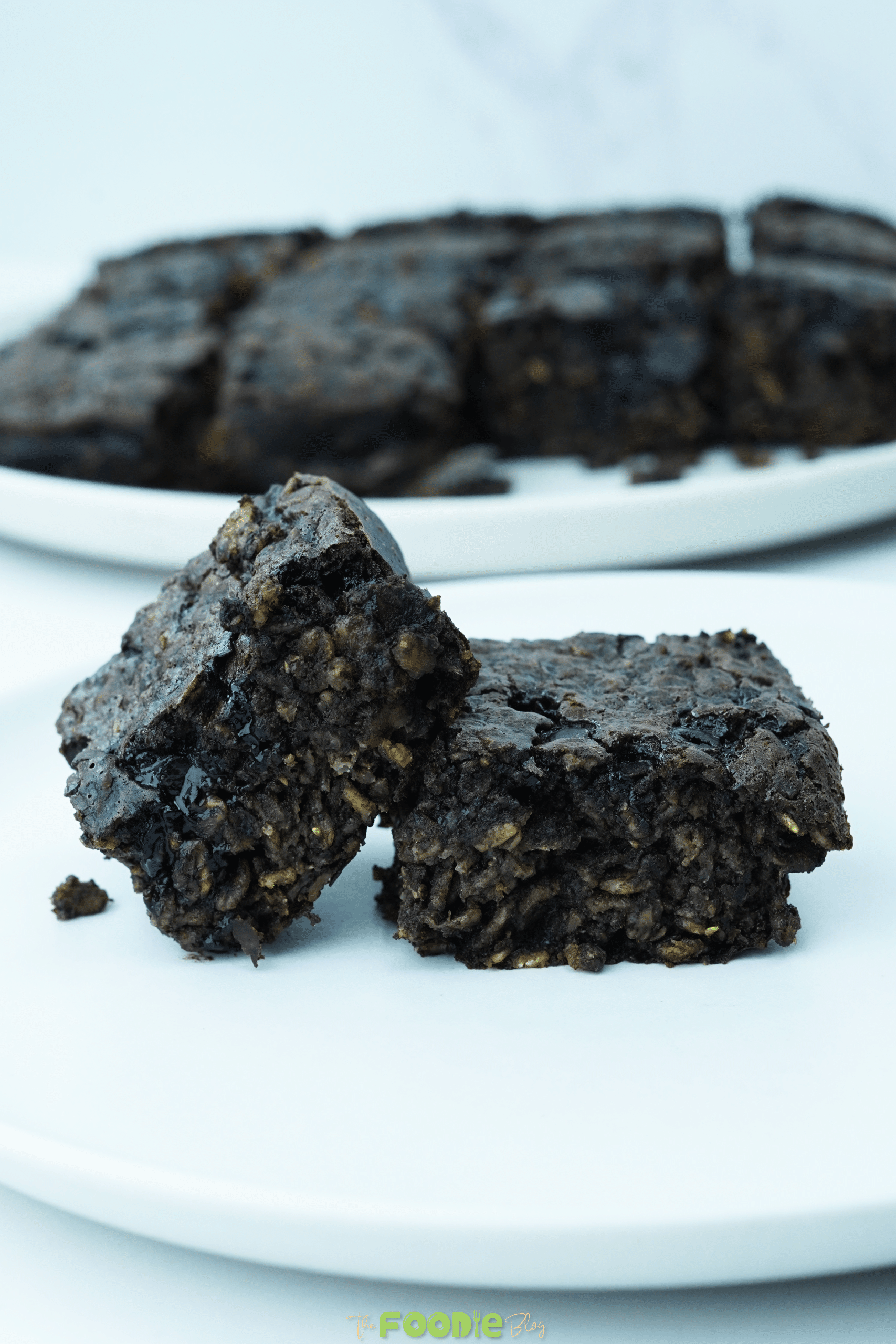 Two oatmeal brownie squares stacked on a white plate