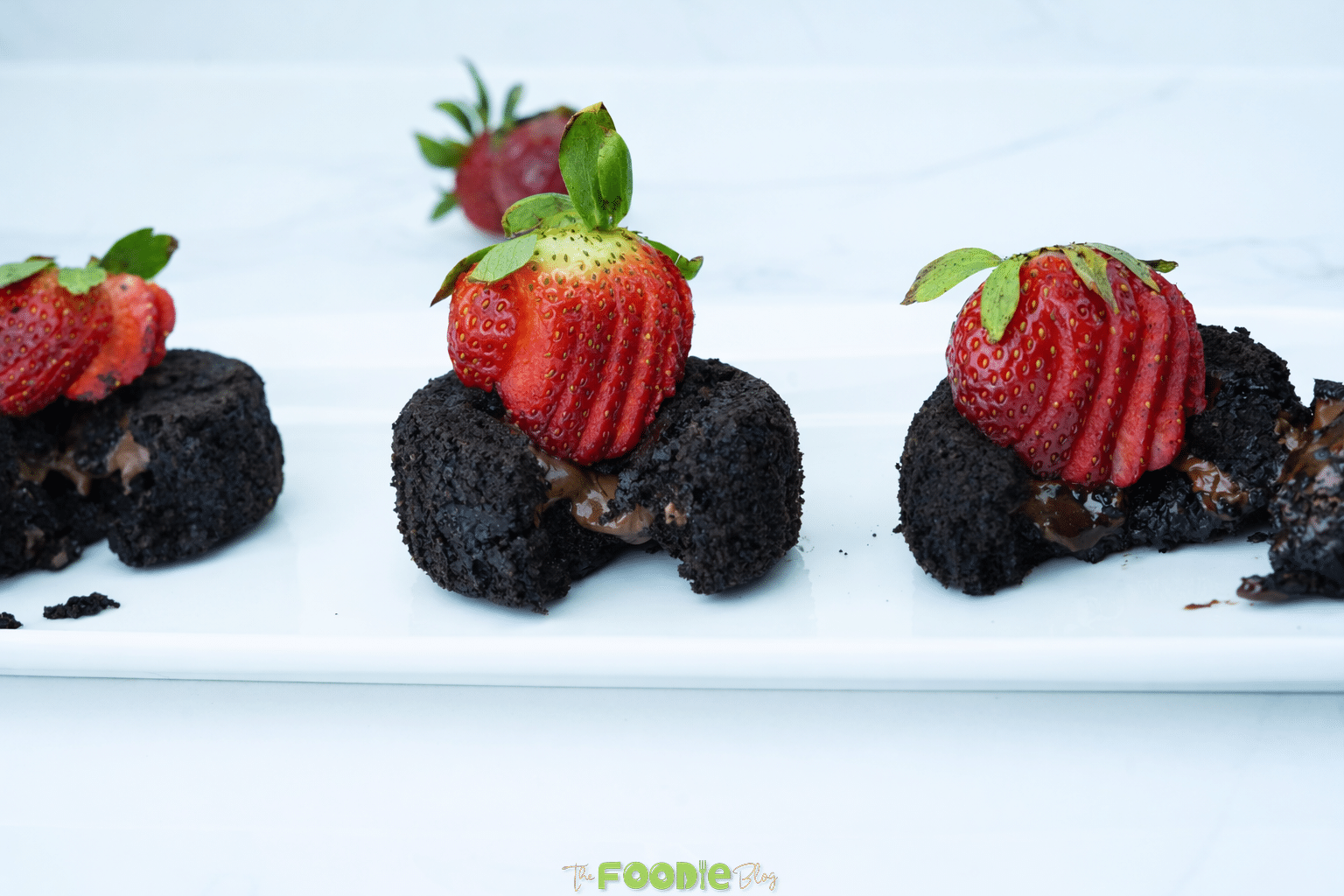 Three mini chocolate lava cakes on a white serving tray with strawberries