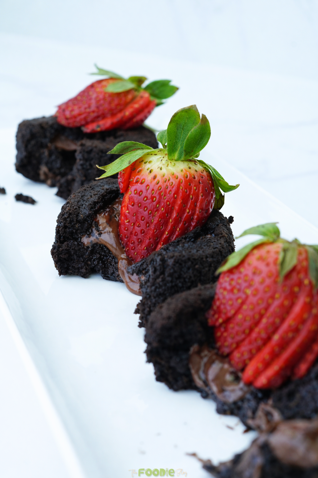 Small chocolate lava cakes topped with sliced strawberries on a white platter