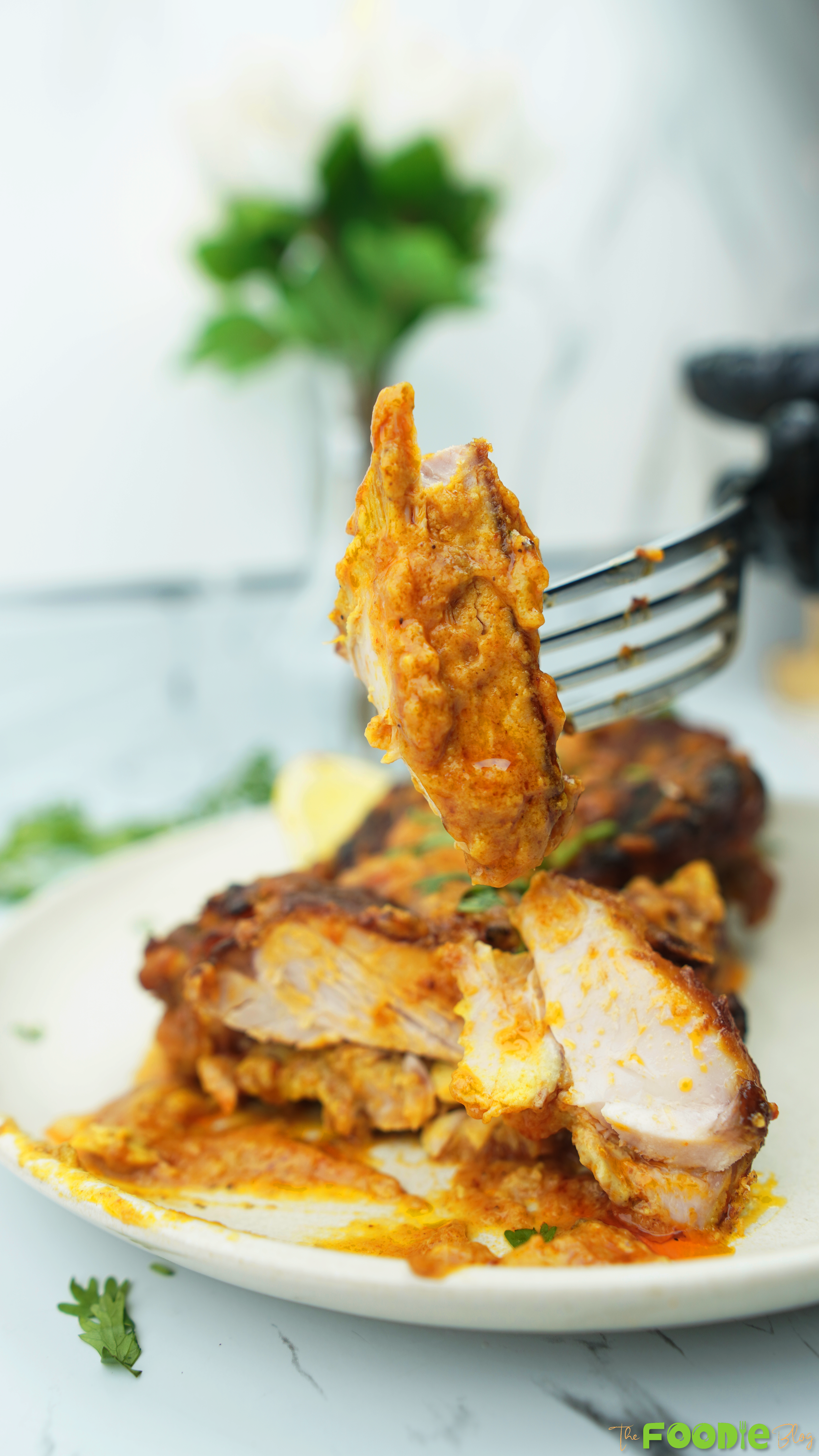 Fork holding a tender bite of butter chicken with creamy orange sauce, with the plate blurred in the background