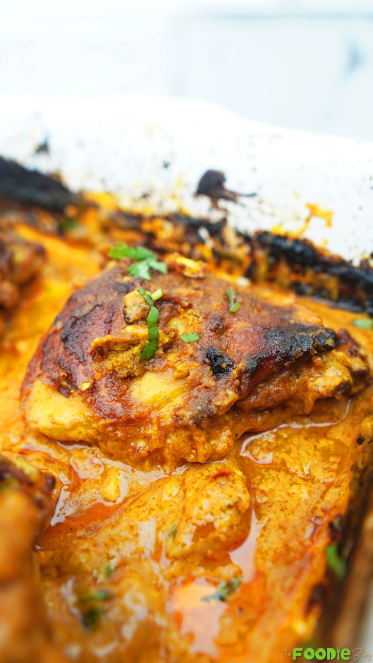 Close-up of baked butter chicken thighs in a creamy tomato sauce inside a baking dish