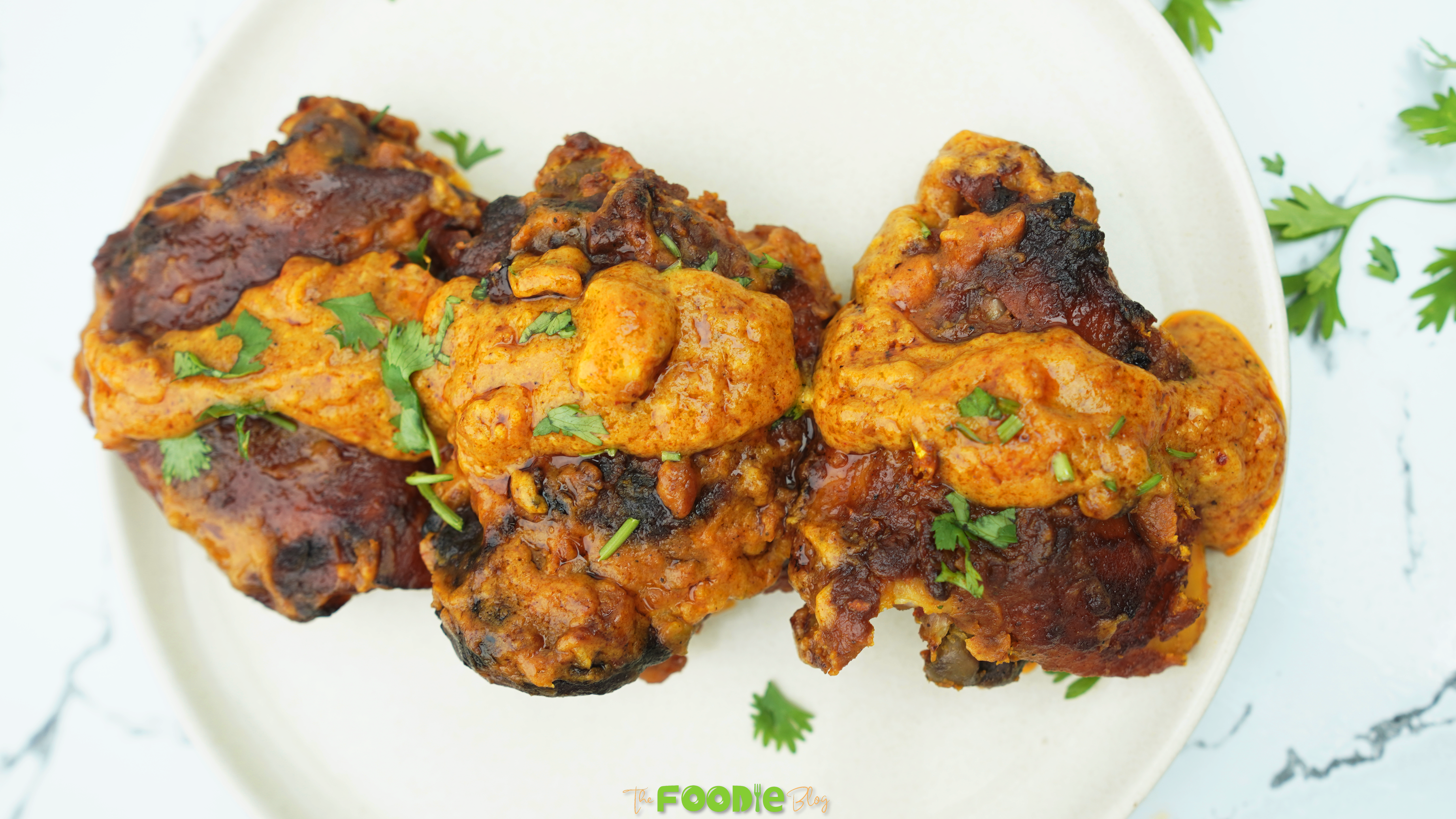 Baked butter chicken thighs coated in creamy tomato sauce on a white plate