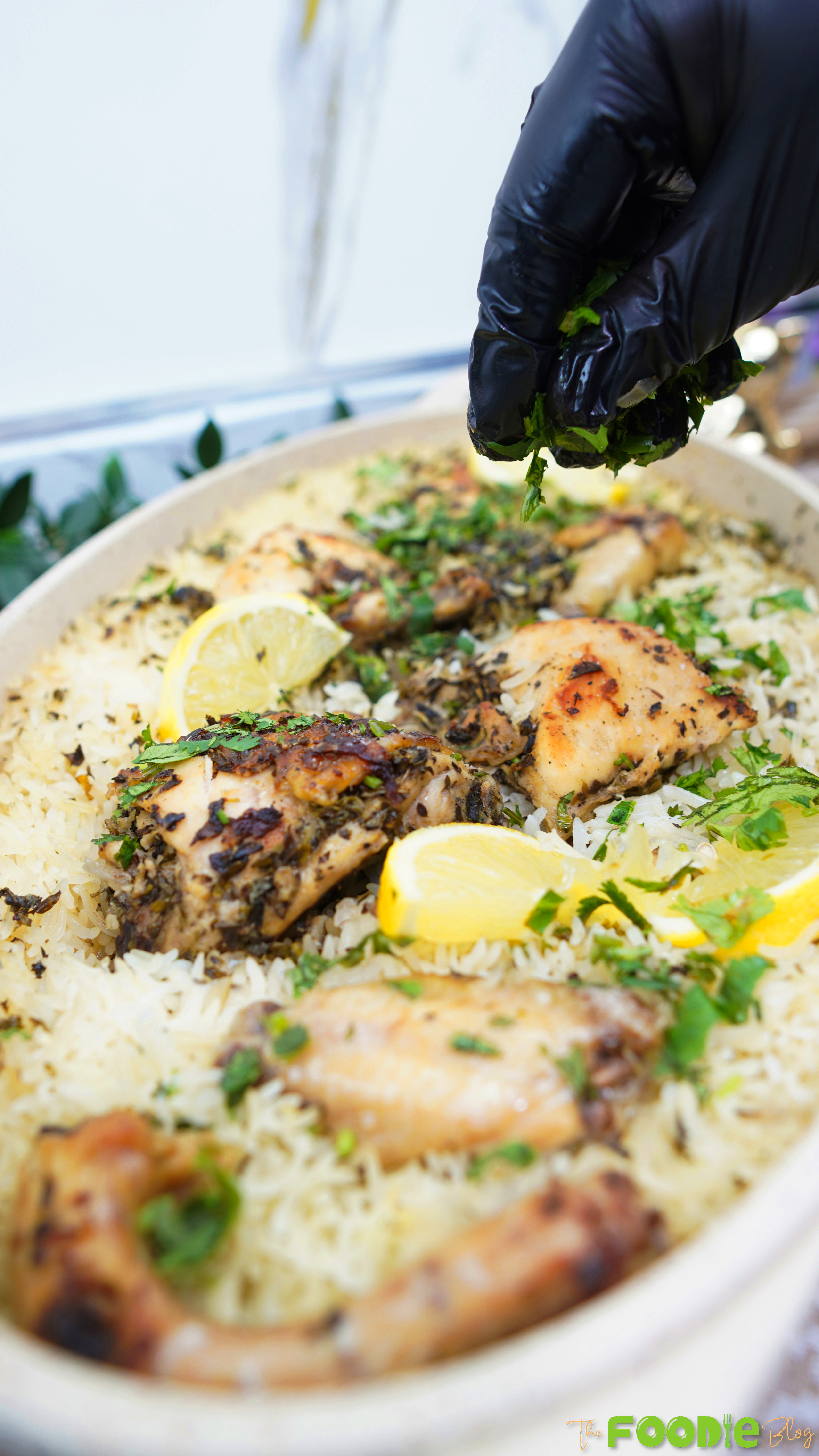 Gloved hand sprinkling chopped parsley over one pot chicken and lemon rice with lemon slices