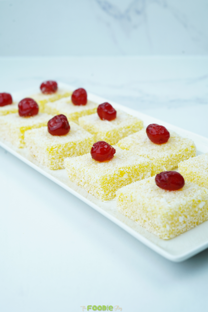 Coconut-coated orange jelly squares topped with candied cherries on a white serving platter