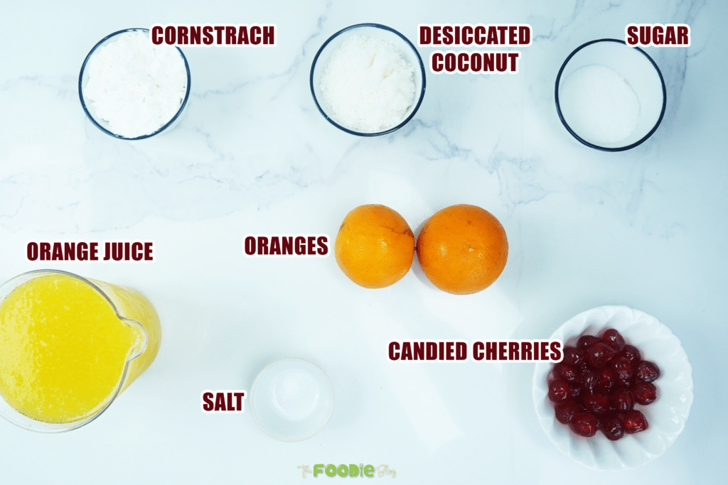 Overhead view of orange juice, oranges, sugar, cornstarch, coconut, salt, and candied cherries for orange jelly