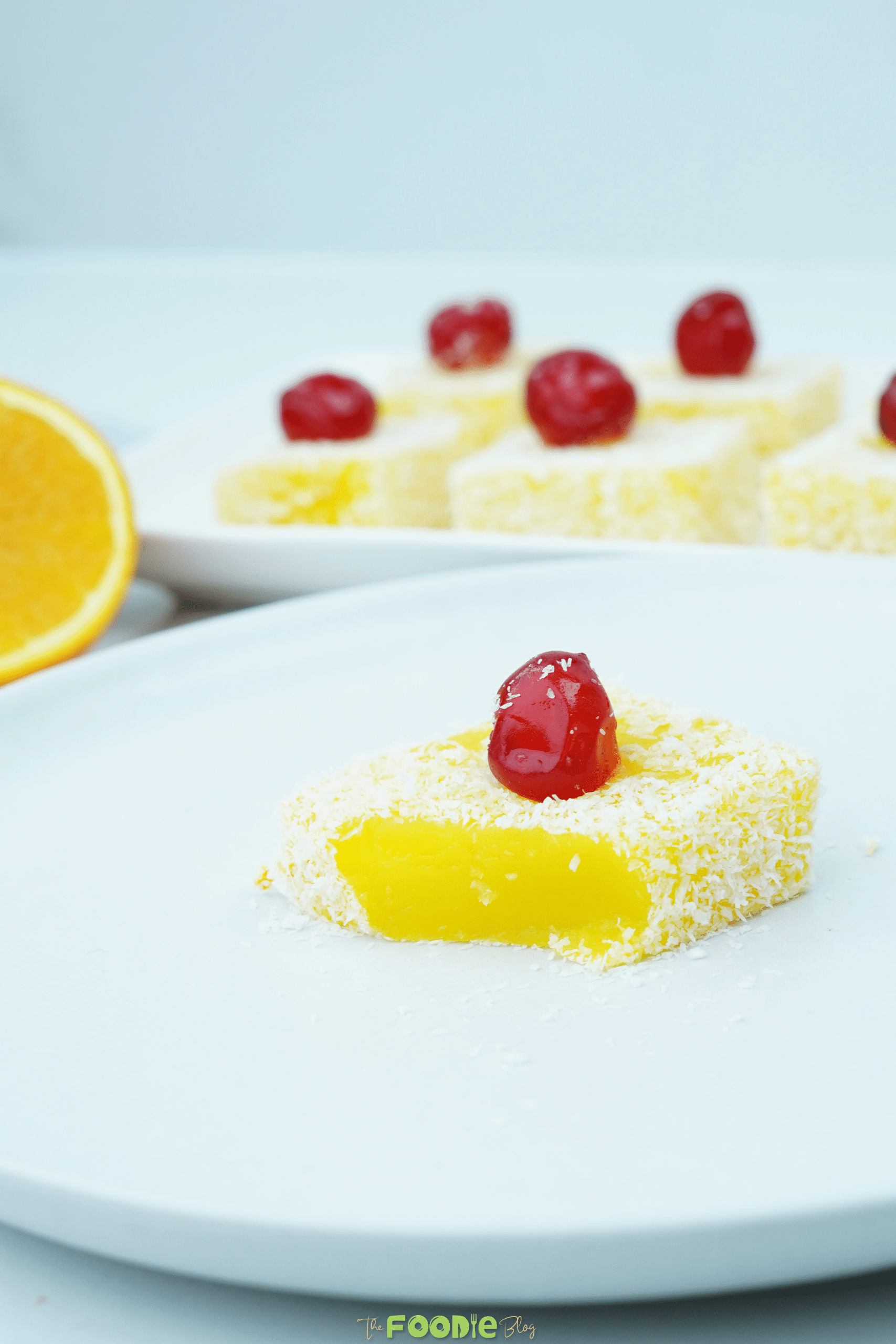 Single orange jelly square coated in coconut with a candied cherry on top on a white plate