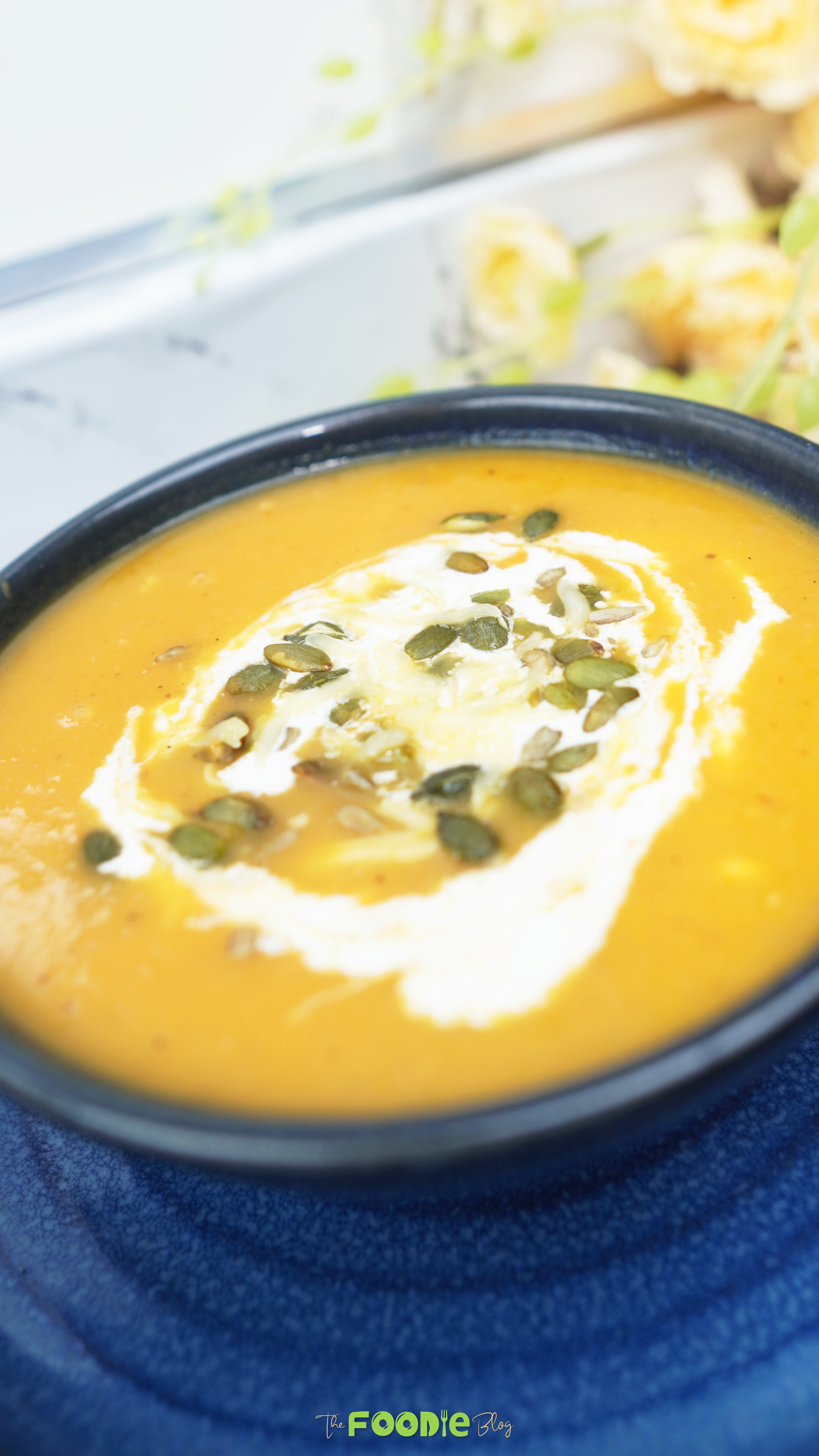 Close-up of oven roasted veggie soup topped with crème fraîche and pepitas in a dark bowl
