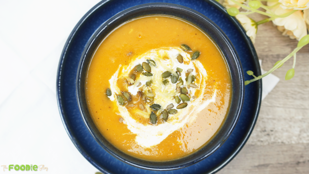 Creamy roasted veggie soup in a blue bowl topped with crème fraîche and pepitas

