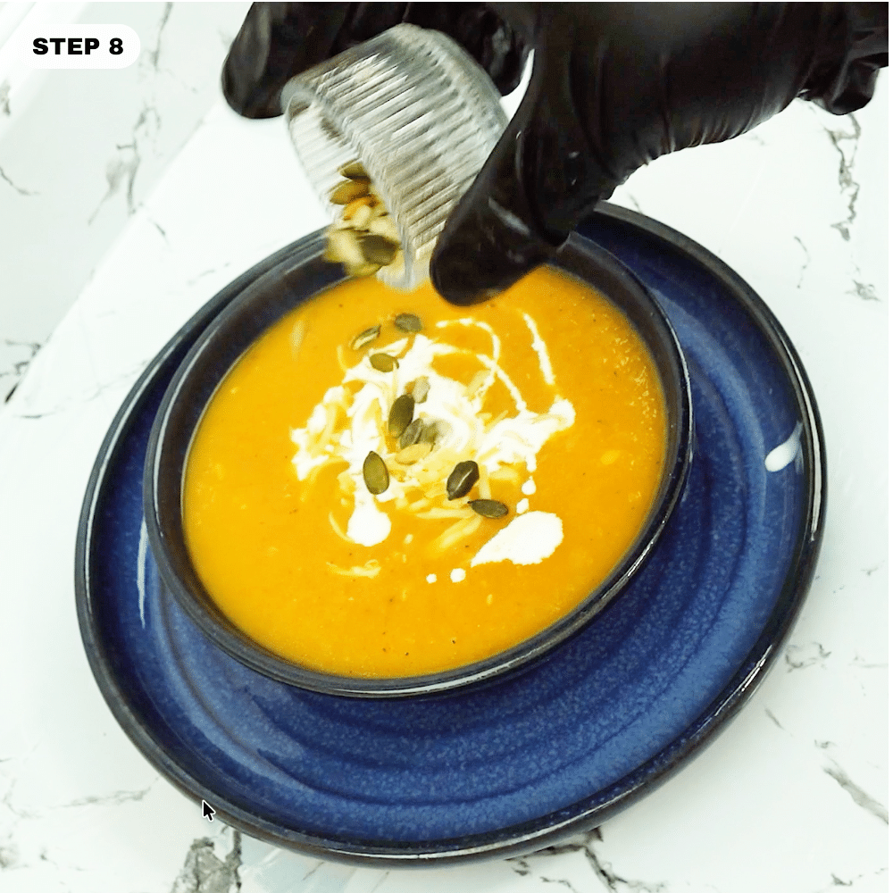 Topping a bowl of roasted veggie soup with pepitas and crème fraîche
