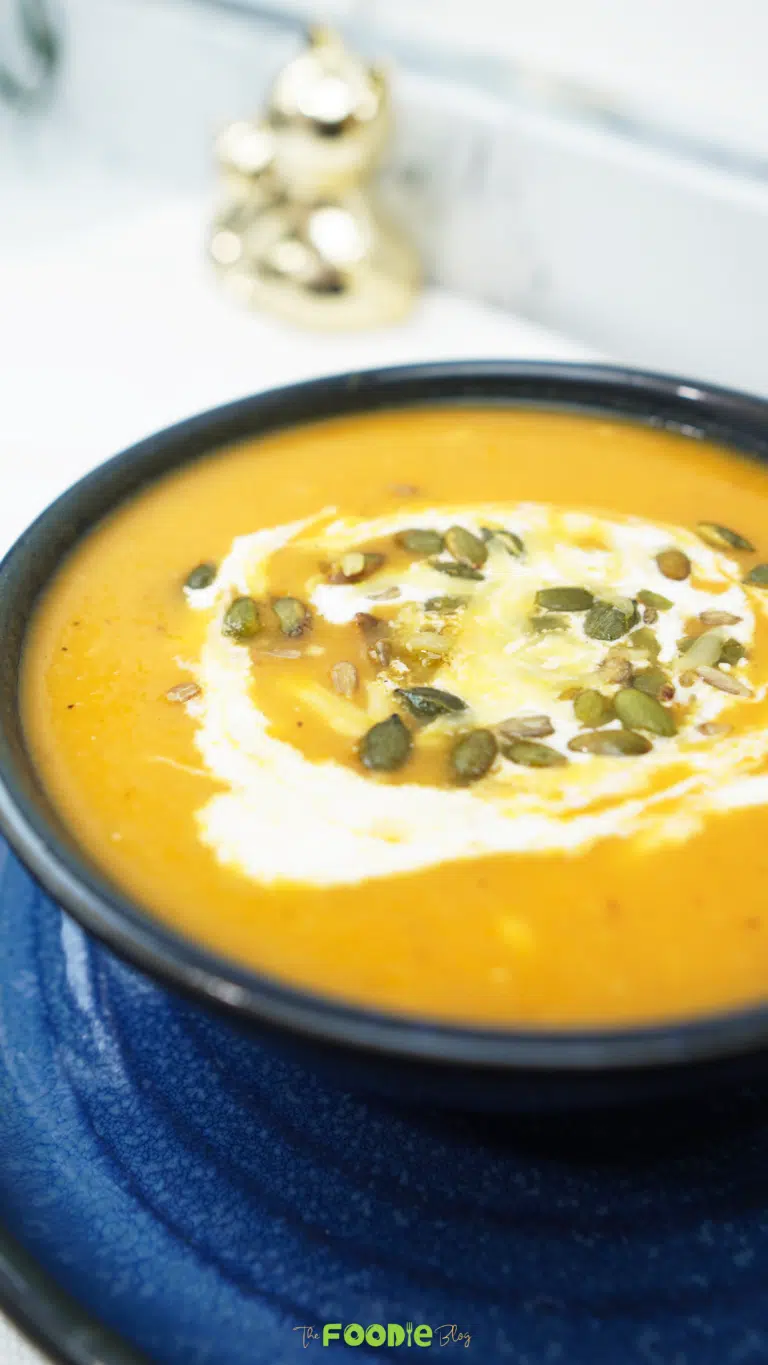Oven roasted veggie soup served in a dark bowl on a blue plate with crème fraîche and pepitas