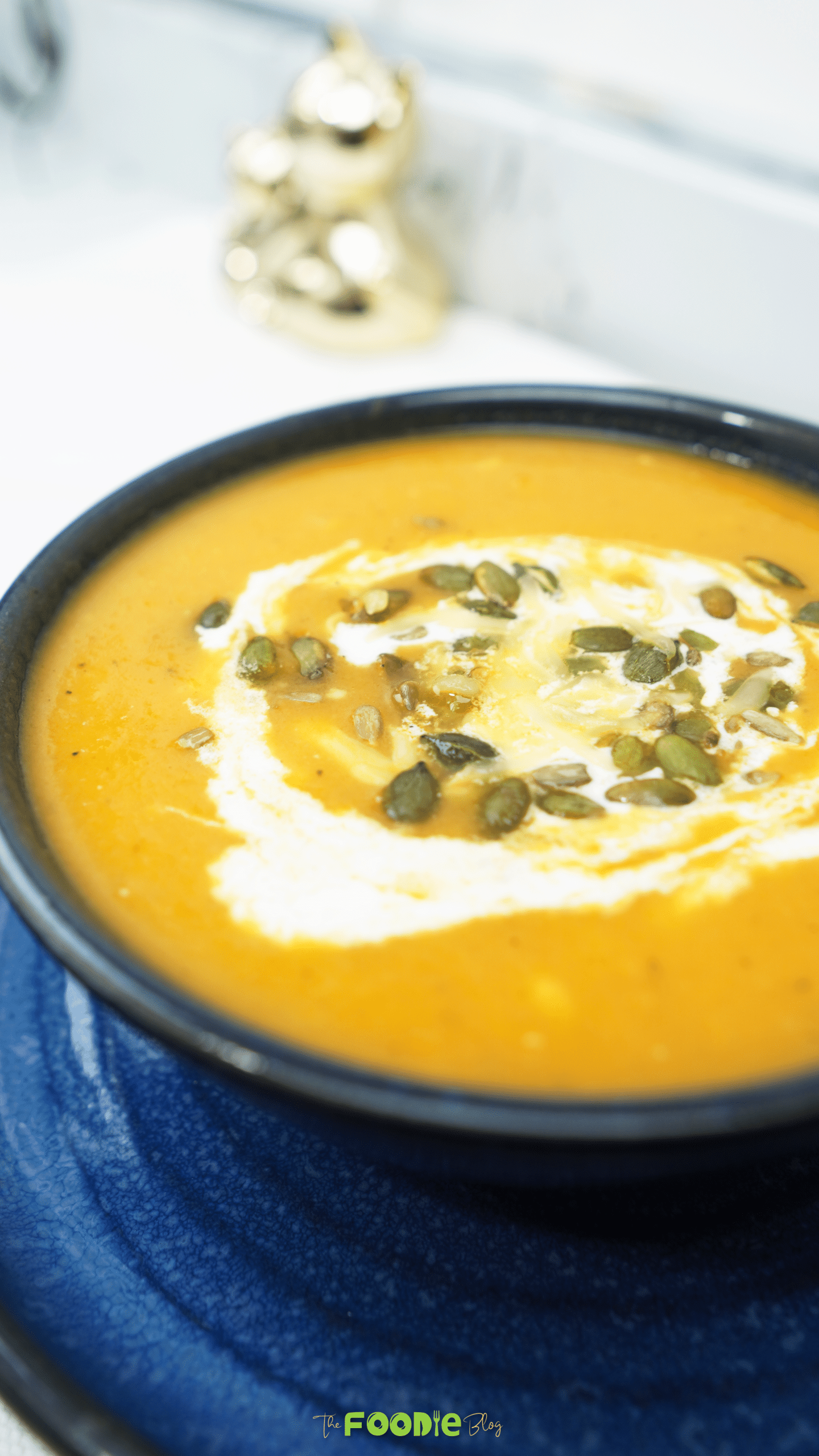 Oven roasted veggie soup served in a dark bowl on a blue plate with crème fraîche and pepitas