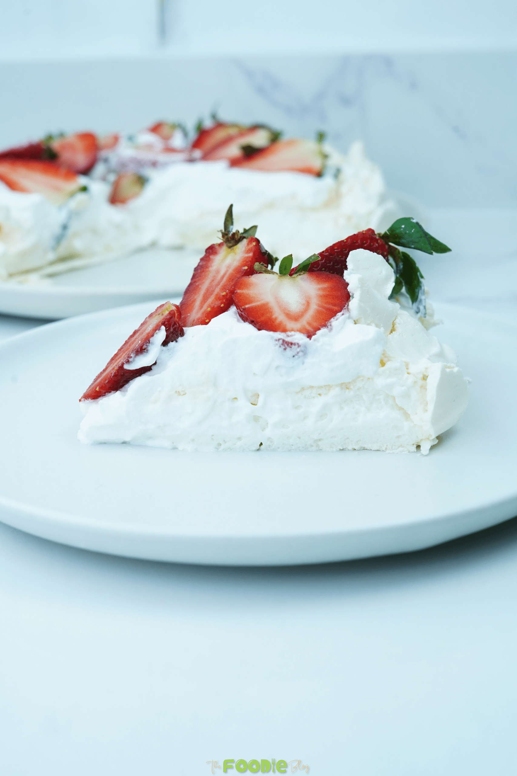 A slice of pavlova on a white plate topped with whipped cream and strawberries