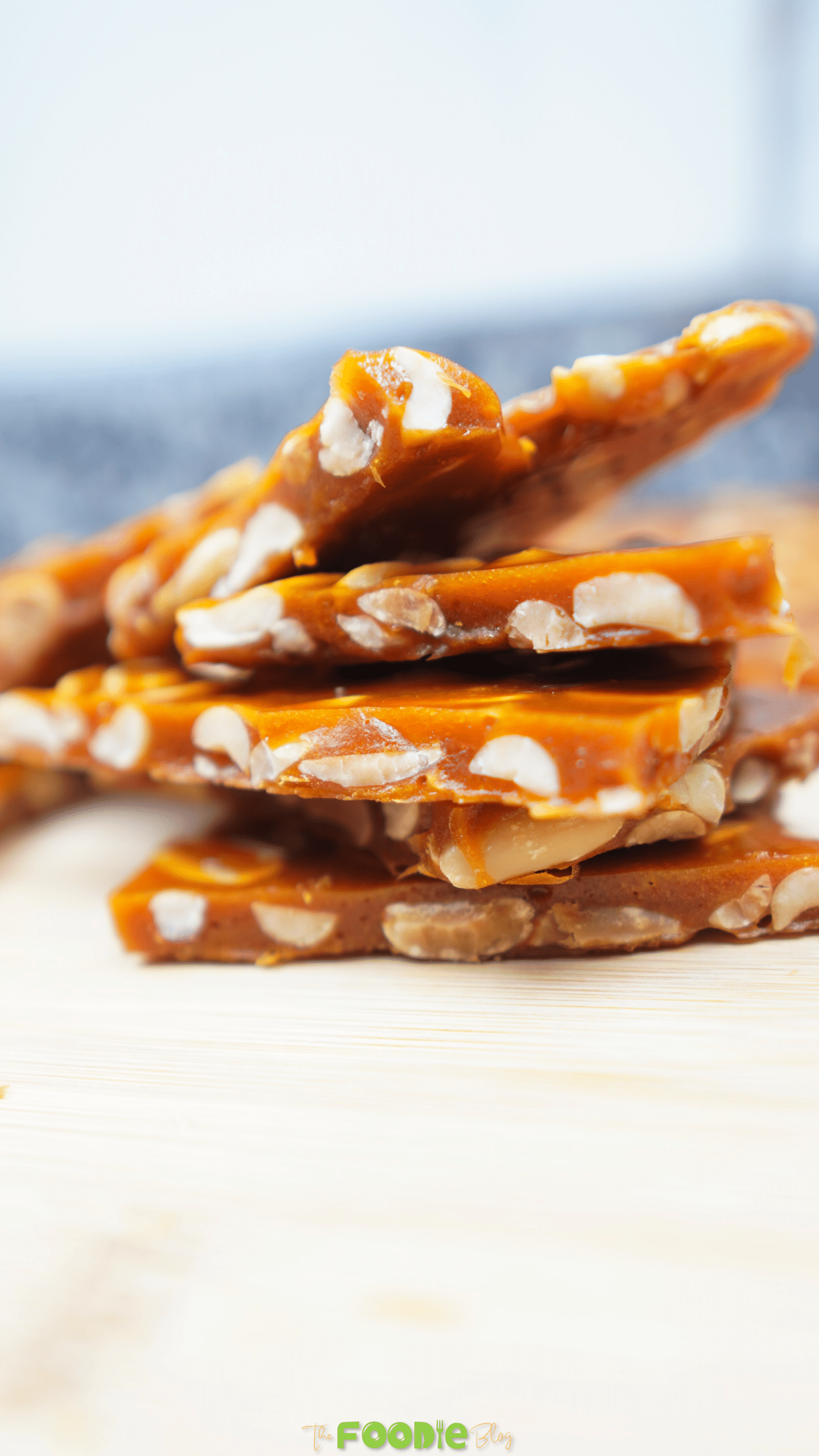 Peanut brittle pieces stacked on a cutting board with a bright, glossy caramel finish