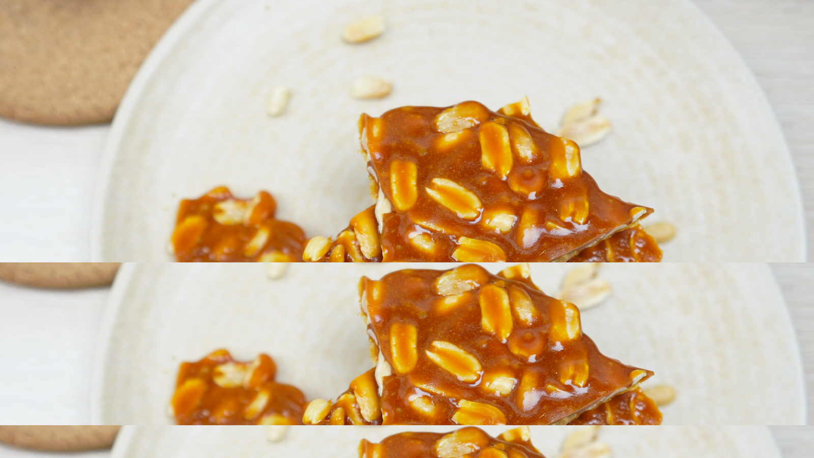 Peanut brittle pieces stacked on a plate with a few peanuts scattered around Caption: Finished peanut brittle ready to serve