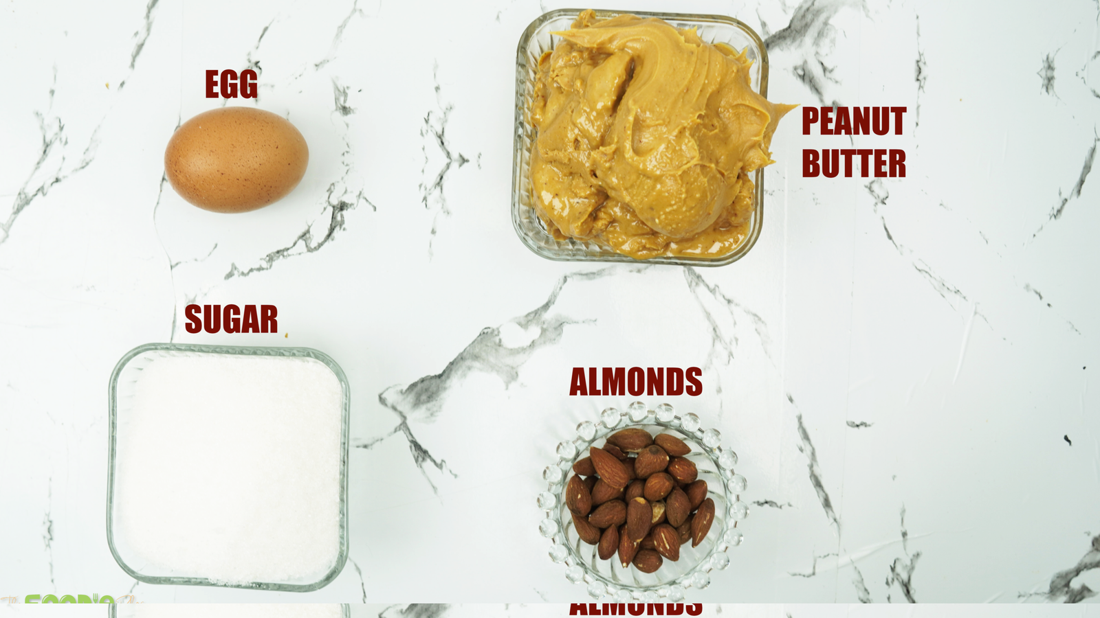 Peanut butter, sugar, egg, and almonds arranged on a counter for baking cookies
