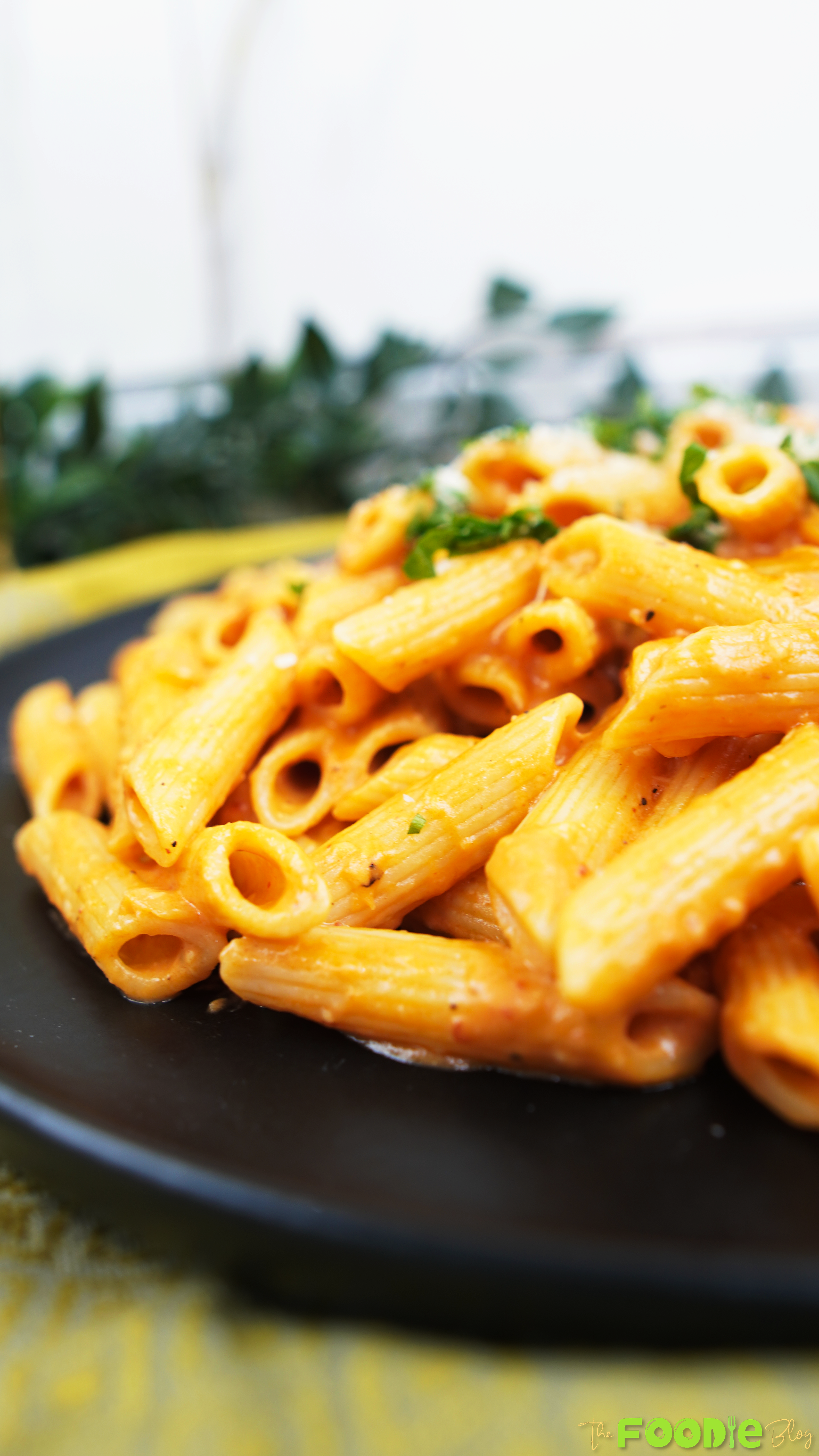 Close-up of penne alla vodka coated in creamy pink vodka sauce, served on a black plate with parsley and parmesan.
