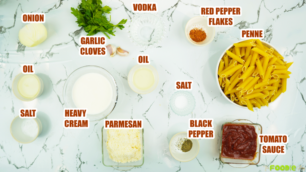Flat lay of penne, heavy cream, tomato sauce, vodka, Parmesan, onion, garlic, and seasonings on a marble surface
