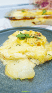 A serving of potatoes au gratin on a dark plate with creamy sauce and a browned top