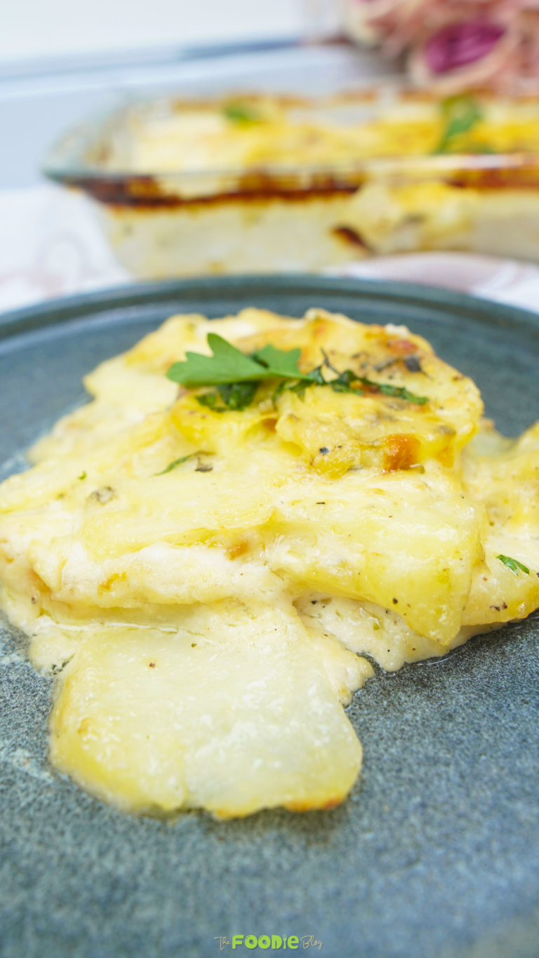 A serving of potatoes au gratin on a dark plate with creamy sauce and a browned top